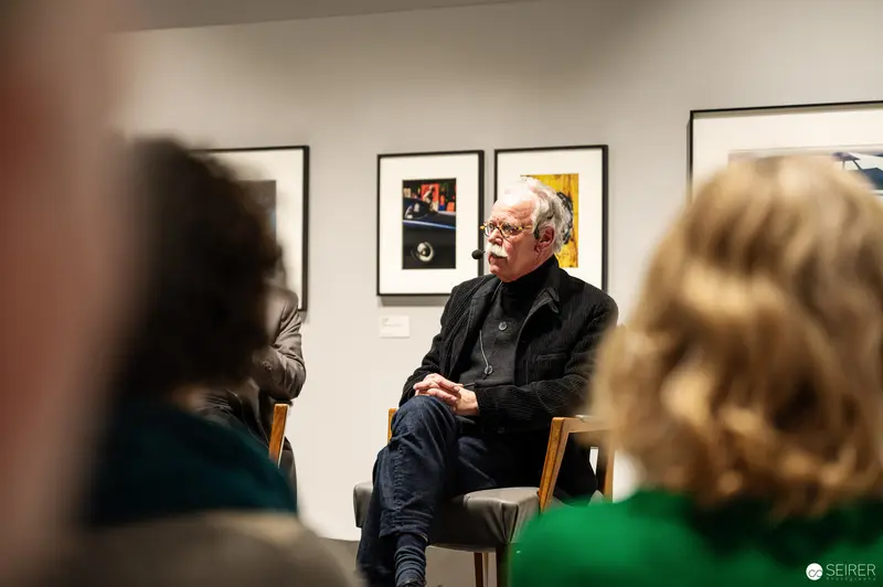Hans-Michael Koetzle Discusses Photography at Gallery Event, Seated Before Framed Artworks