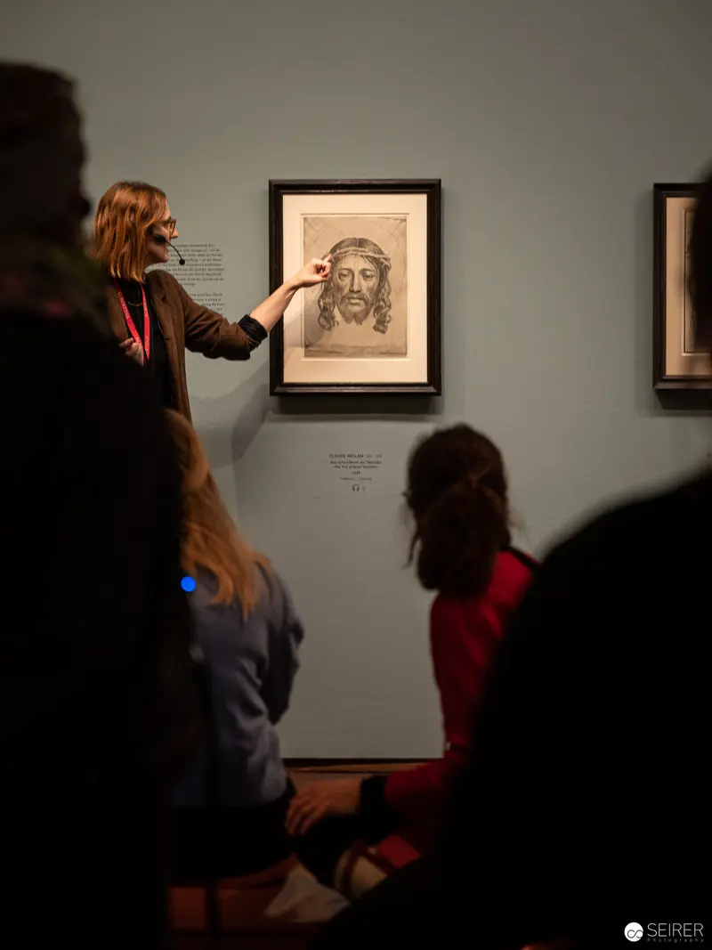 Docent Gesturing Towards Framed Artwork During Dürer, Munch, Miro Exhibition