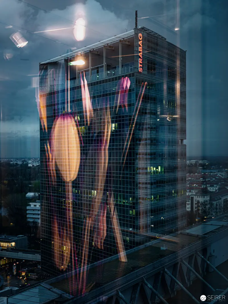 Reflective Glass Tower with Luminous Tulip Projections in Urban Landscape