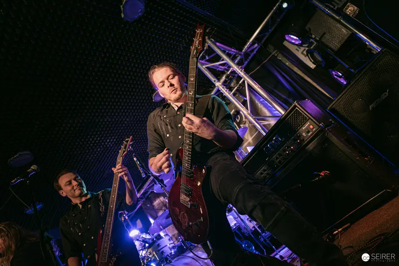 Guitarists Performing Under Blue Stage Lights at Replugged Vienna
