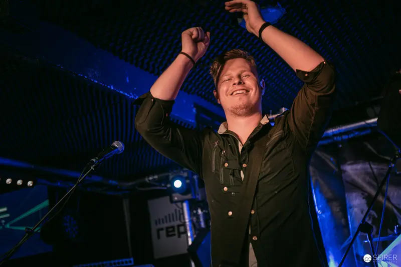 Triumphant Performer at Replugged Vienna Under Blue Atmospheric Lighting
