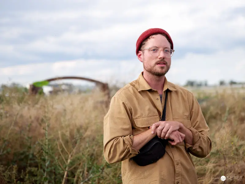 Urban Agricultural Guide in Autumn Grasslands Wearing Ochre Overshirt and Red Beanie
