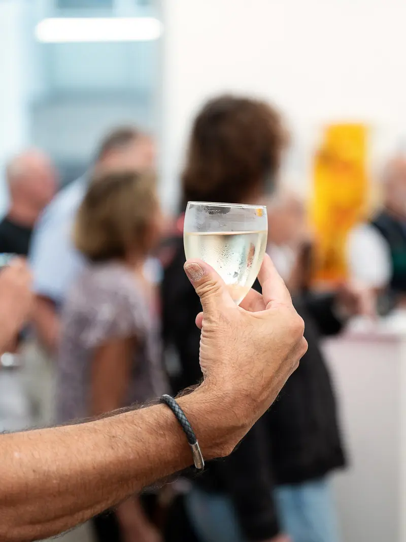 Hand Holding Wine Glass at Social Gathering with Blurred Guests