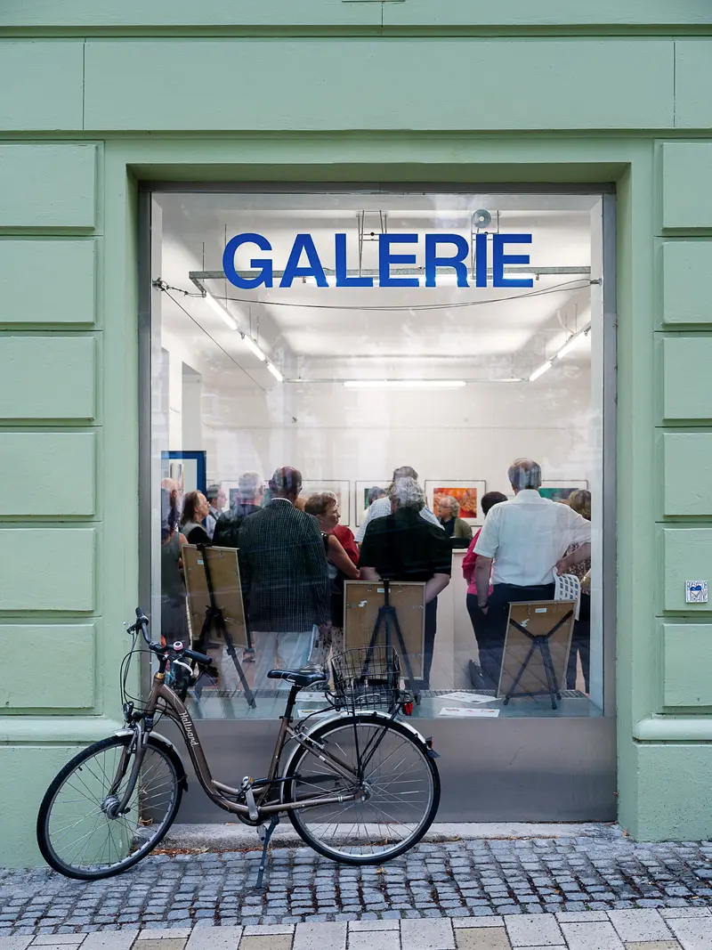 Visitors Observing Art Exhibition Through Gallery Window with Parked Bicycle