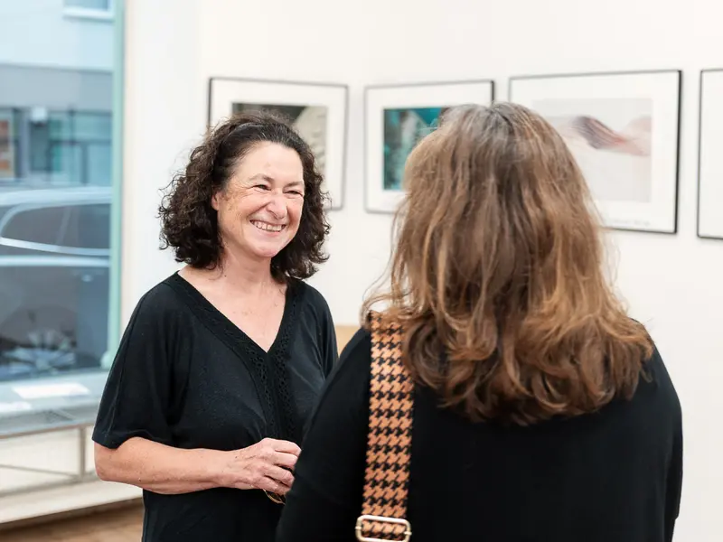 Gallery Interaction: Two Women in Conversation amid Framed Artwork