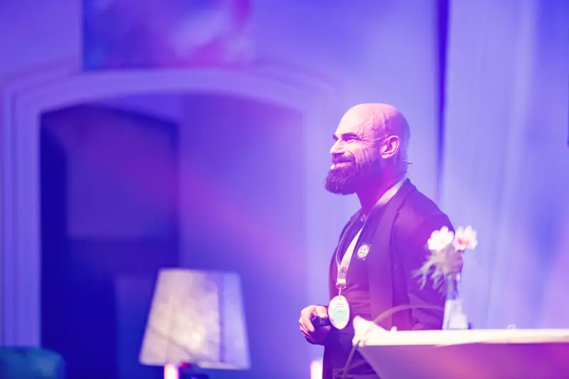 Bald Speaker Radiates Passion Under Purple Lighting at Health & Mind Festival