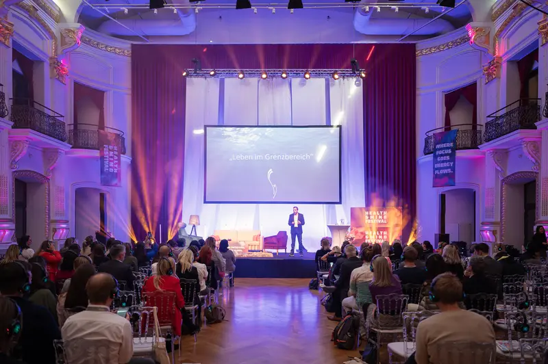 Health & Mind Festival: Presenter Illuminated on Stage in Purple-Hued Venue
