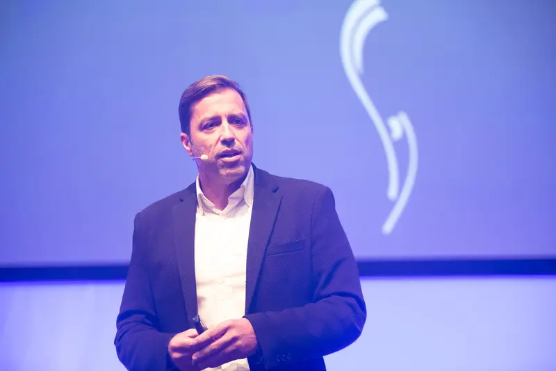 Speaker at Health & Mind Festival Presents on Stage with Minimalist Blue Background
