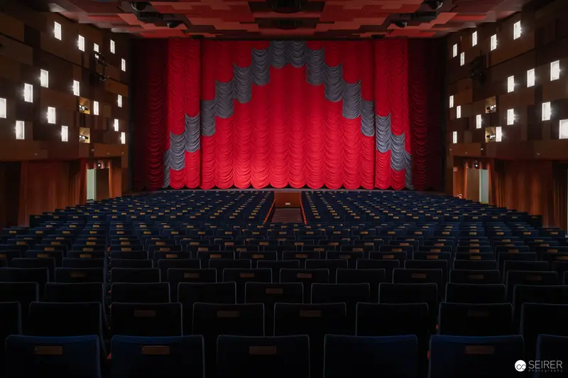 Empty Cinema Hall with Vibrant Red Curtained Stage and Blue Seating