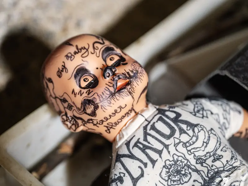 Intricately Tattooed Doll with Skull-Like Facial Markings on Textured Surface