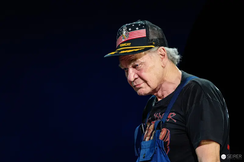 Veteran in Patriotic Cap Reflects Pensively on Dark Stage