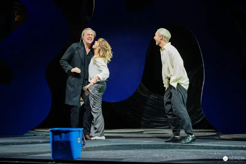 Elmar Goerden's Lulu: Three Performers on Minimalist Stage with Blue Backdrop