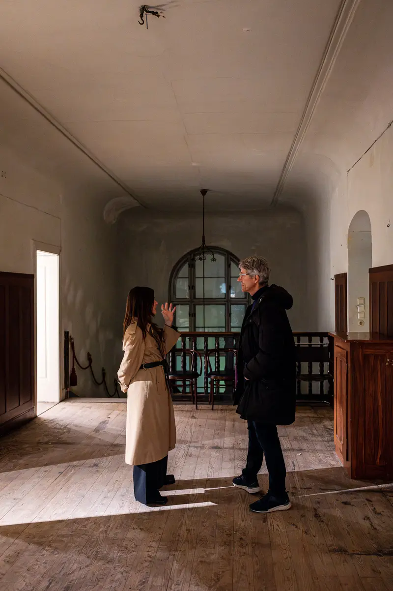 Two Figures in Sparse Interior, Sunlight Dividing Wooden Floor Space