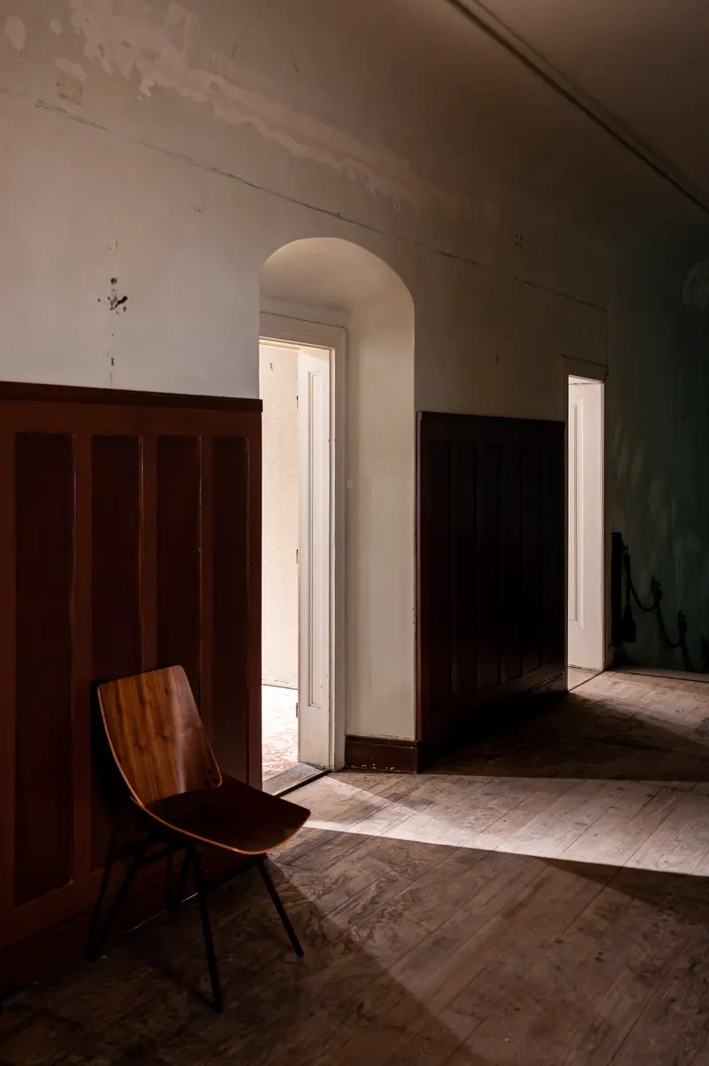Solitary Wooden Chair in Shadowed Interior with Arched Doorway and Wooden Paneling