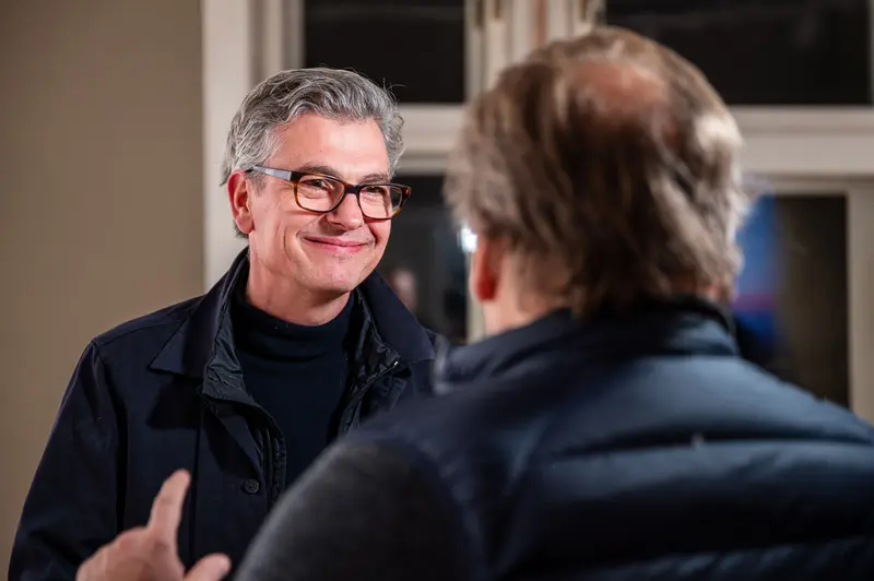 Two Professionals in Conversation Near Window in Subdued Interior Setting