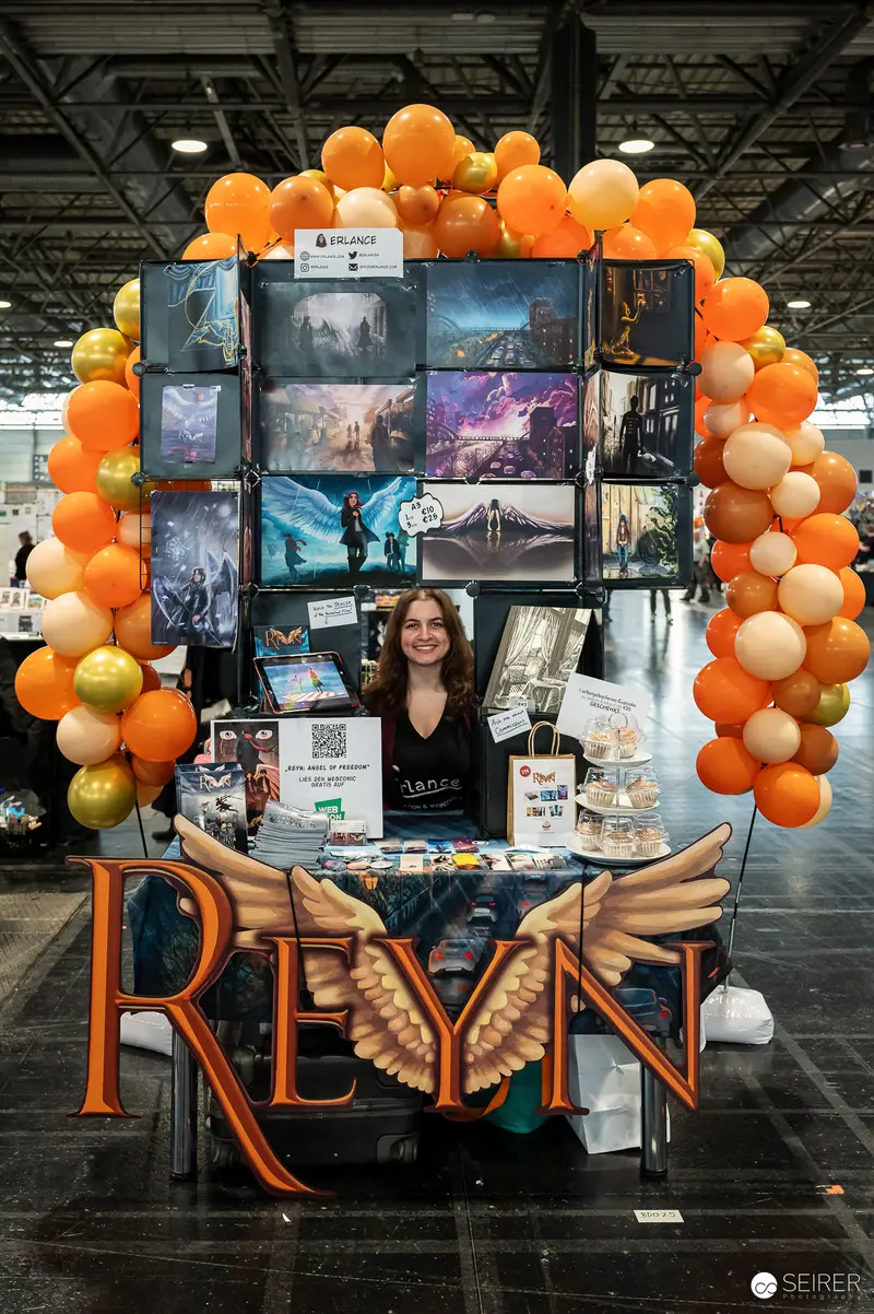 Artist Showcasing Fantasy Artwork at Convention with Balloon-Framed Display