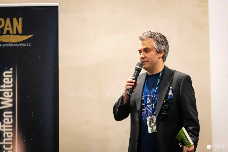 Speaker Presenting at VIECC Comic Convention with Microphone and Book