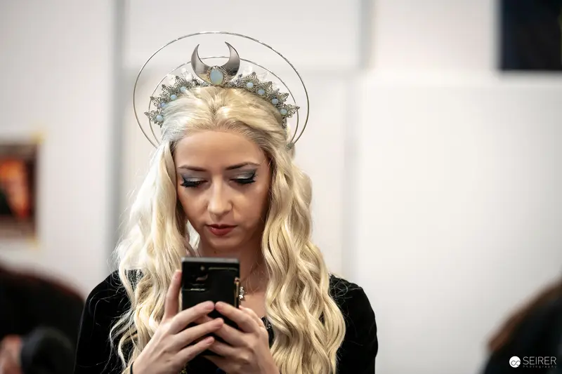 Cosplayer with Crescent Moon Tiara Engaged with Mobile Device at Vienna ComicCon 2023