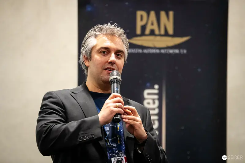 PAN Event Speaker in Black Blazer Addressing Audience with Microphone