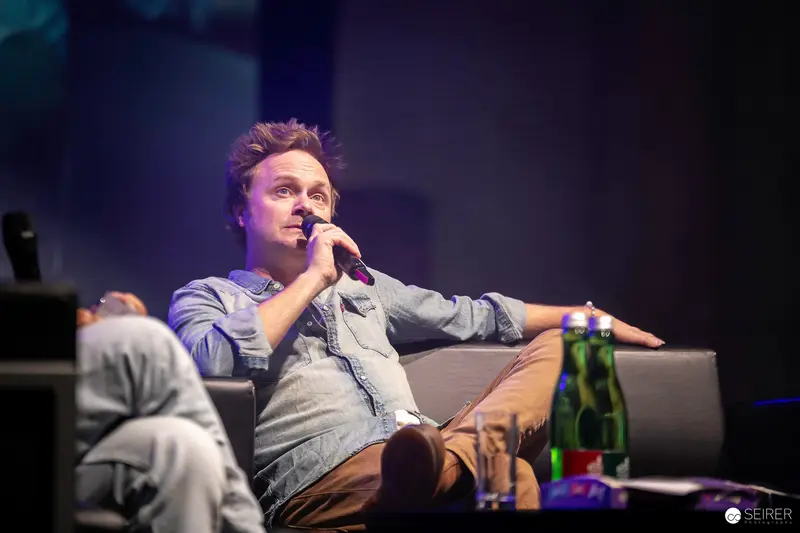 Performer in Denim Jacket Seated Casually During Stage Interview