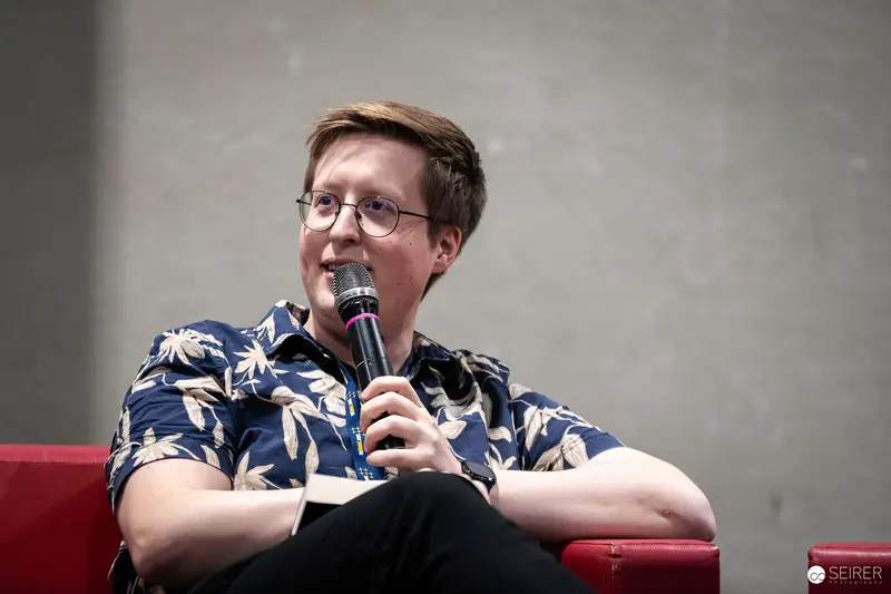 Vienna ComicCon 2023: Speaker in Floral Shirt Addresses Audience with Microphone