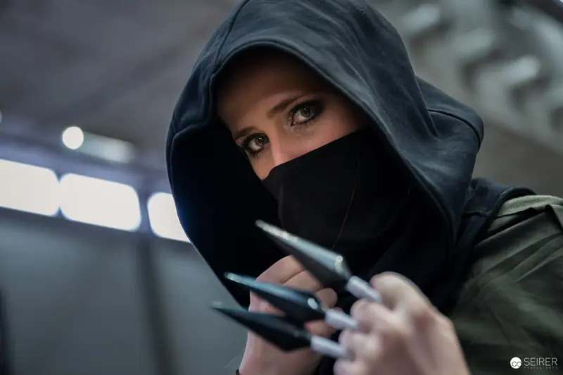 Hooded Figure with Intense Gaze Holding Tactical Implement in Dramatic Lighting