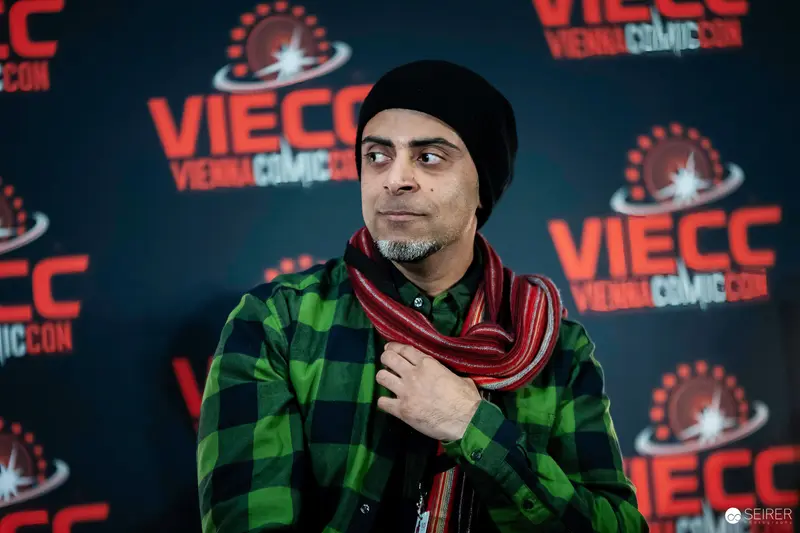 Subject Posing at Vienna ComicCon 2023 Press Wall in Plaid and Beanie