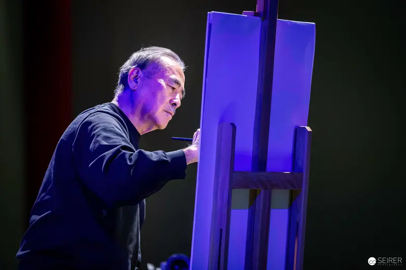 Artist Painting Intently on Illuminated Blue Canvas During Performance