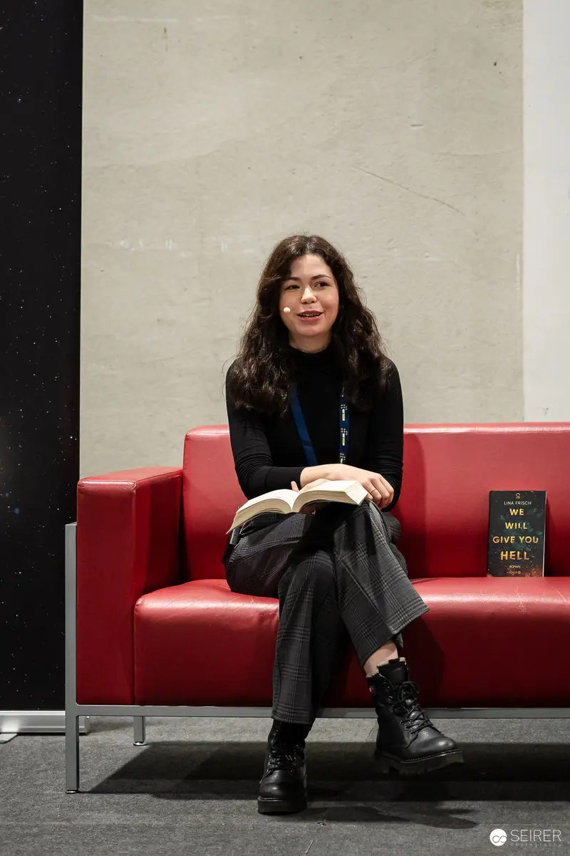 Reader in Black Seated on Red Couch with Open Book