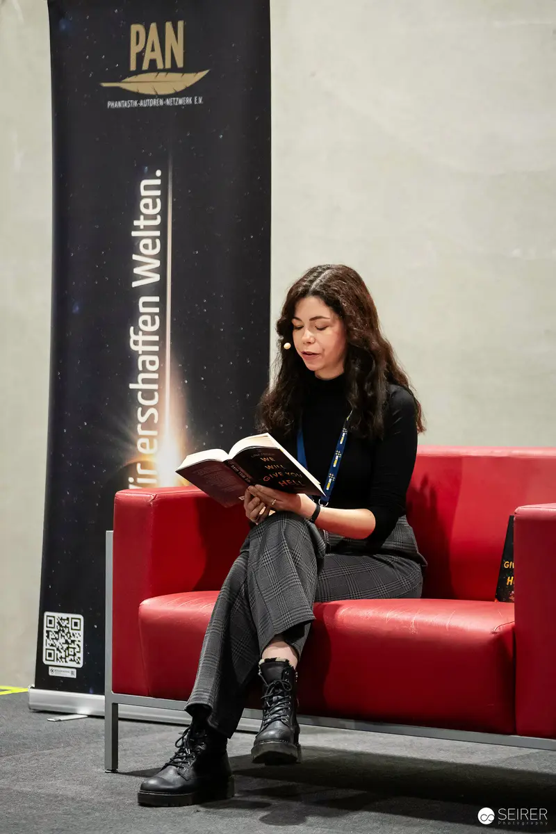 Young Woman Absorbed in Reading at PAN Event on Red Couch