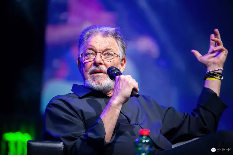 Bearded panel guest speaking into handheld microphone on stage at VIECC Vienna Comic Con 2023