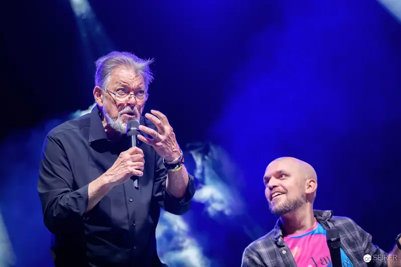 Elderly guest speaker with microphone on VIECC Vienna Comic Con panel stage, November 2023