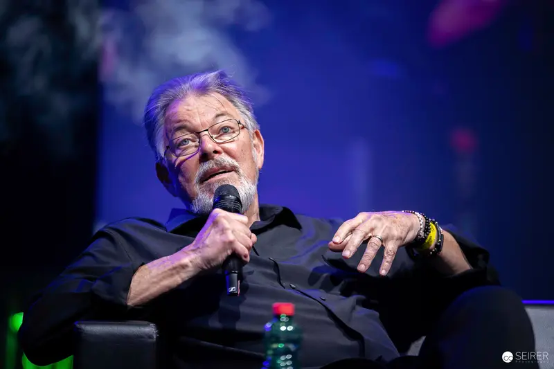 Bearded panel guest speaking into handheld microphone onstage at VIECC Vienna Comic Con 2023
