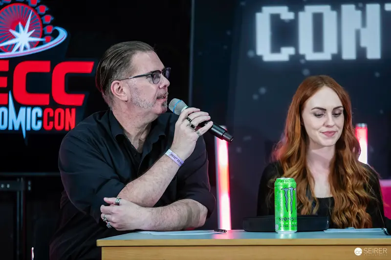 Panel speaker with microphone beside red-haired panellist at VIECC Vienna Comic Con 2023