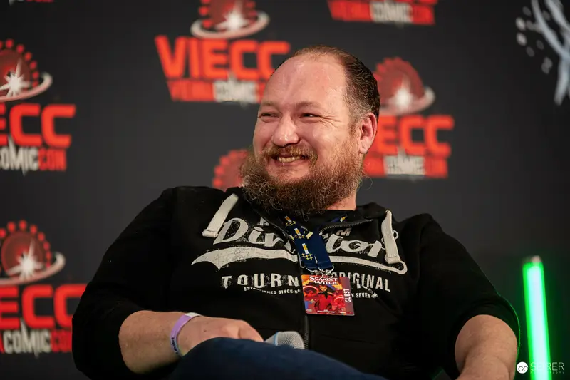 Bearded panel guest laughing on stage in front of VIECC Vienna Comic Con backdrop