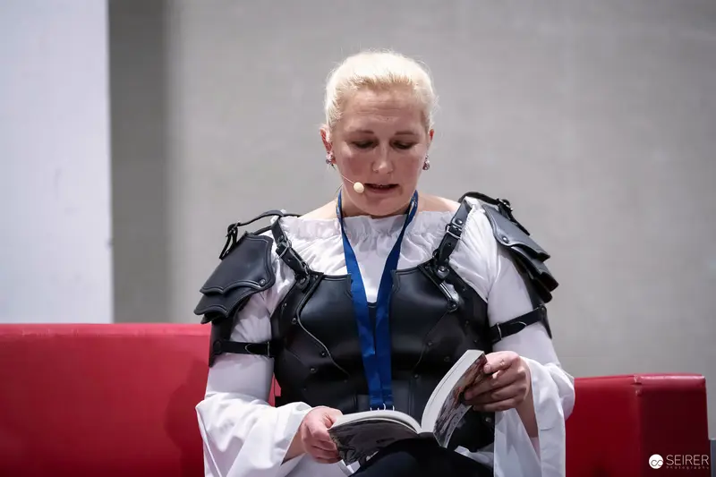 Author in leather armour and headset microphone reads from book at VIECC Vienna Comic Con 2023