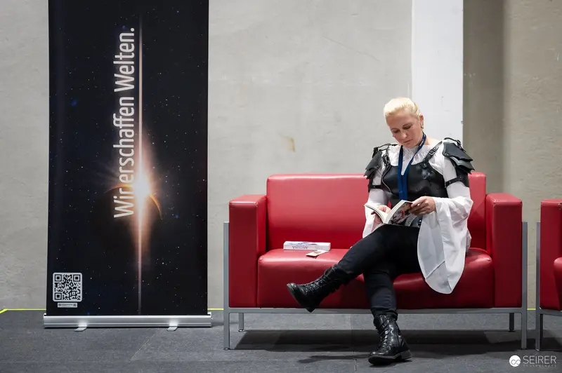 Cosplayer in Armour Reads Programme on Red Sofa at VIECC Vienna Comic Con 2023