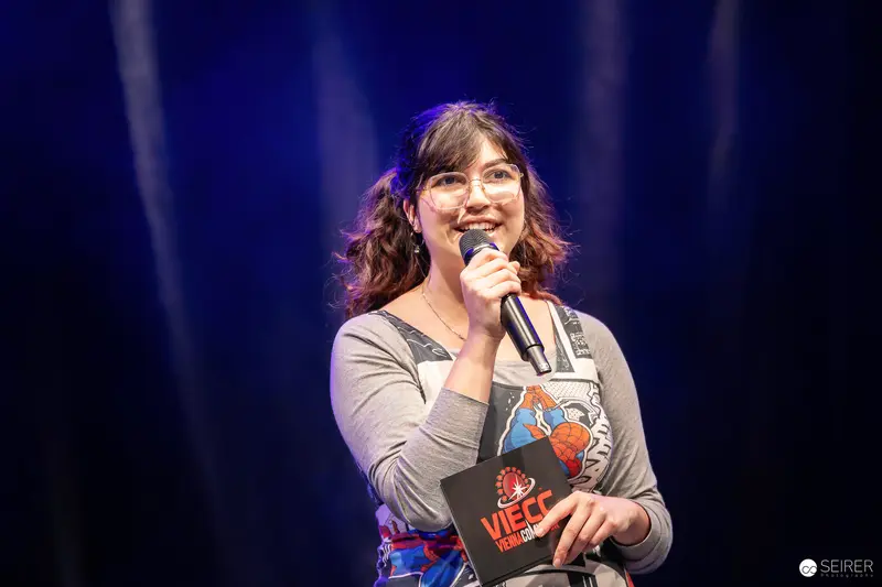 Host with VIECC-branded clipboard speaks on stage at Vienna Comic Con 2023