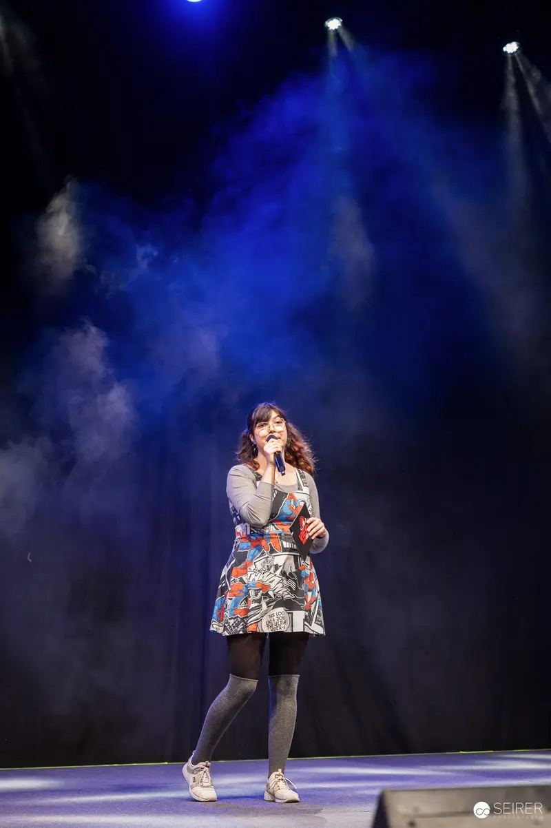 Host in comic-print dress with microphone on main stage at VIECC Vienna Comic Con 2023