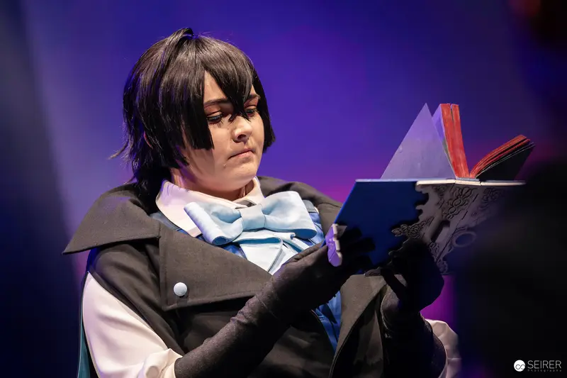 Cosplayer in Black Cape Reading Prop Book on VIECC Vienna Comic Con Stage