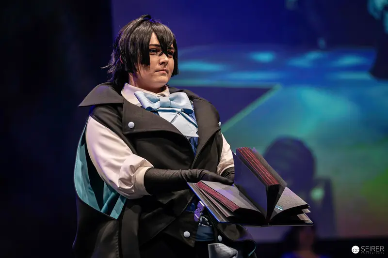 Cosplayer in Black Caped Costume Holding Prop Book on Stage at VIECC Vienna Comic Con 2023