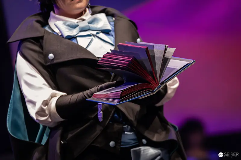Cosplayer Holding Open Book Prop on Stage at VIECC Vienna Comic Con 2023