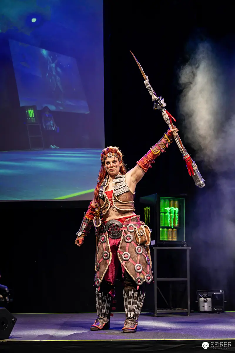 Cosplayer raises spear in armoured costume on VIECC Vienna Comic Con stage, November 2023