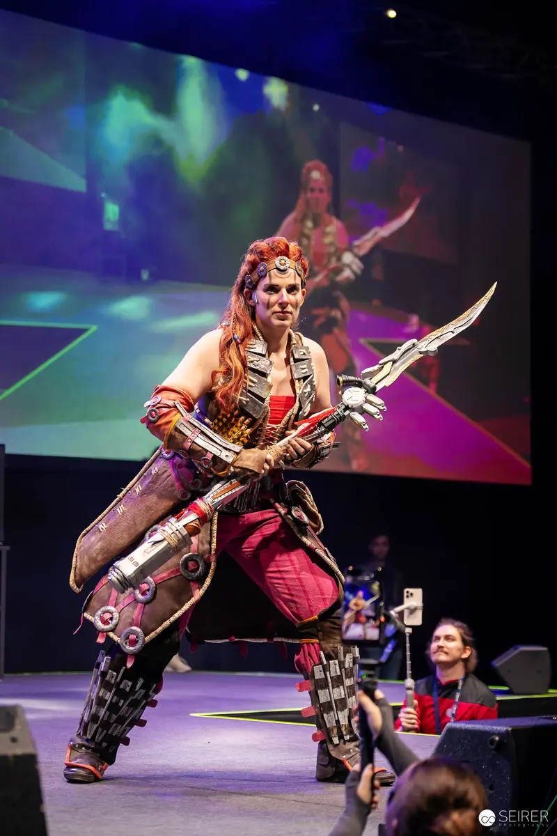 Aloy cosplayer from Horizon poses with spear on VIECC Vienna Comic Con stage
