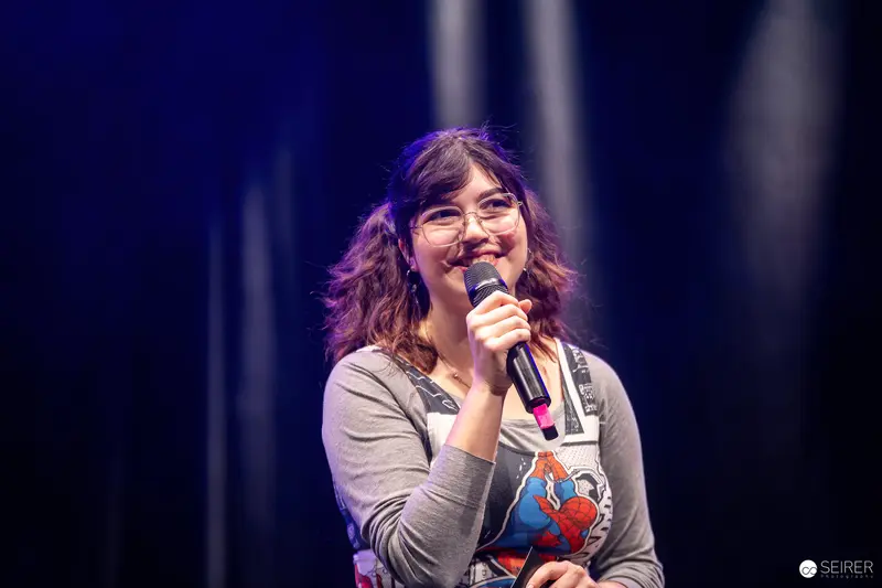Smiling host with handheld microphone on stage at VIECC Vienna Comic Con 2023
