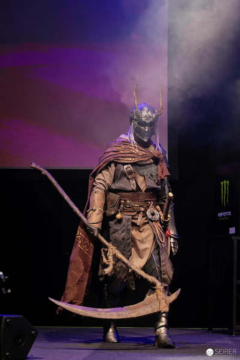 Antlered Masked Warrior Cosplayer with Double-Bladed Scythe on VIECC Vienna Comic Con Stage
