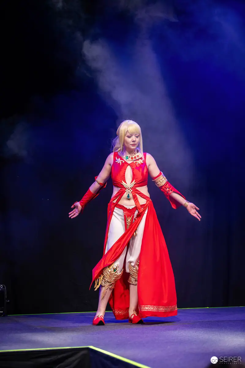 Cosplayer in red and gold fantasy costume performing on stage at Vienna Comic Con 2023