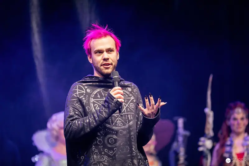 Pink-haired host with microphone presenting cosplay contest on stage at VIECC Vienna Comic Con 2023