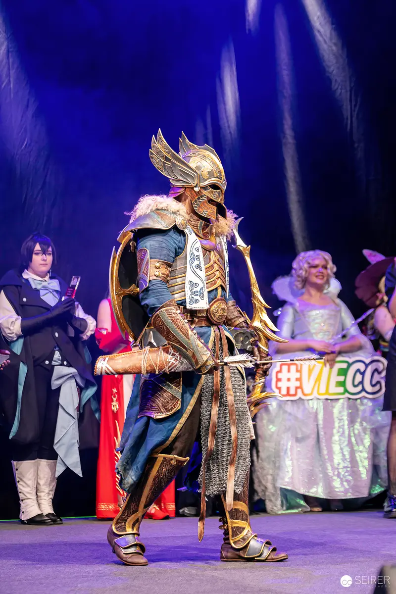 Winged-Helm Archer Cosplayer with Golden Bow on VIECC Vienna Comic Con Stage
