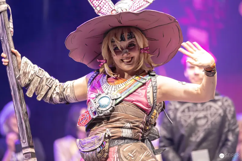 Cel-shaded Borderlands-style cosplayer with wide-brim hat waving on VIECC Vienna Comic Con stage